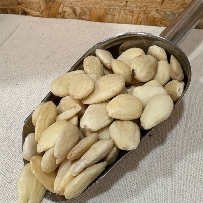 Colher metálica com amêndoas sem casca sobre superfície clara e fundo de madeira