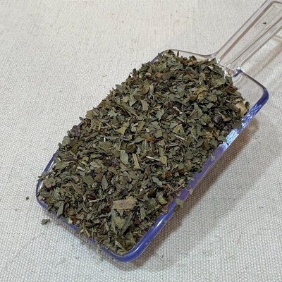 Colher de plástico com folhas secas verdes e castanhas sobre tecido bege