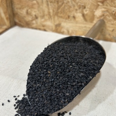 Pá metálica cheia de sementes pretas pequenas sobre superfície branca e fundo de madeira.