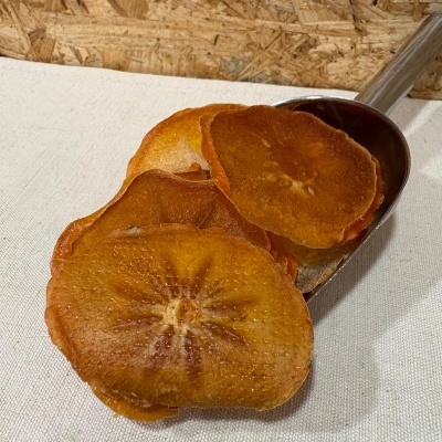 Fatias de fruta desidratada laranja em colher metálica sobre fundo branco e parede de madeira