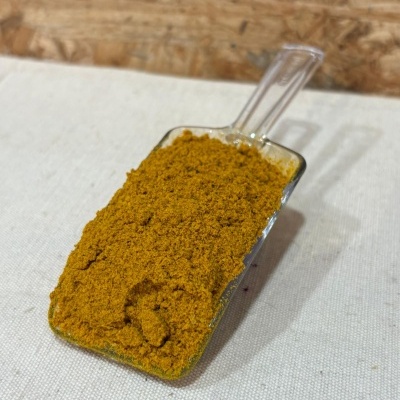 Pá transparente com especiaria em pó amarelo-laranja sobre tecido branco e fundo de madeira.