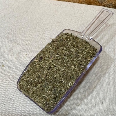 Pá transparente com ervas secas verdes sobre tecido claro e fundo de madeira