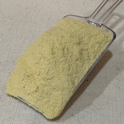 Pá plástica transparente com pó amarelo claro sobre superfície bege texturada