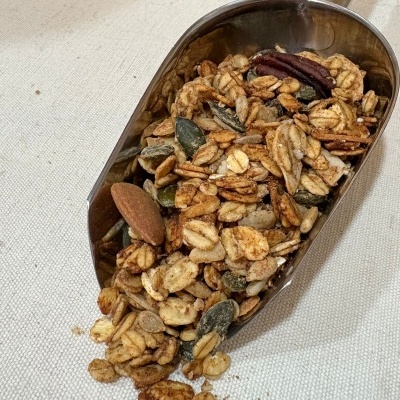 Colher metálica com granola mista contendo aveia, sementes e nozes sobre tecido bege claro