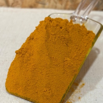 Espátula de vidro com pó laranja-amarelado sobre tecido branco.