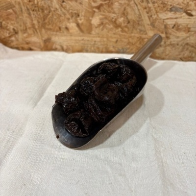 Colher metálica com ameixas secas sobre tecido bege e fundo de madeira