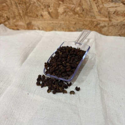 Pá transparente com grãos pequenos escuros sobre tecido branco e fundo de madeira aparente