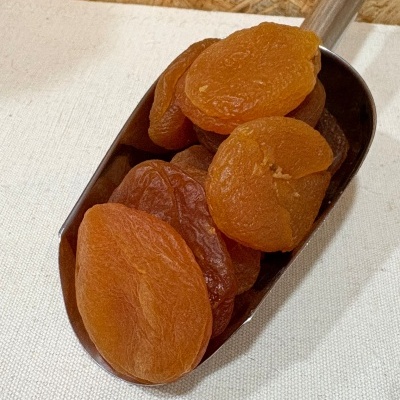 Damasco seco laranja numa colher metálica sobre superfície branca com fundo de madeira clara