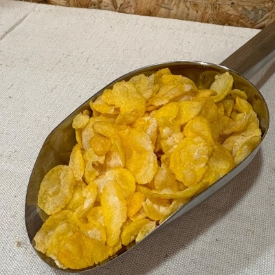 Pá metálica com flocos de cereais de milho amarelos sobre tecido branco