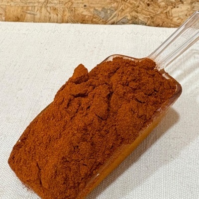 Pá cheia de pó castanho-avermelhado sobre superfície branca com fundo de madeira