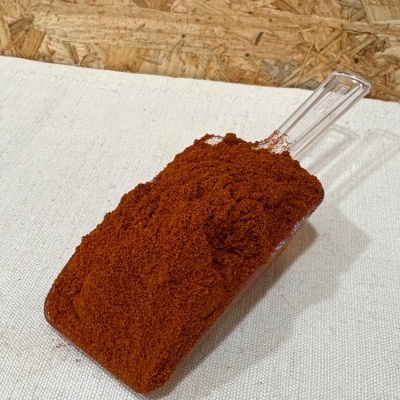 Pá de plástico com pó vermelho sobre tecido branco e fundo de madeira.