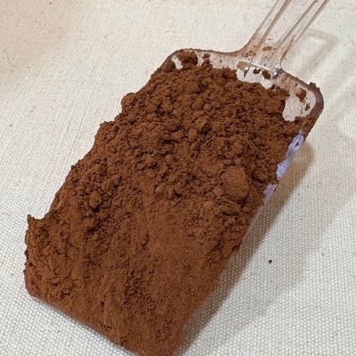 Pá transparente cheia de pó castanho escuro sobre superfície clara.