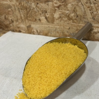 Colher metálica com grânulos amarelos sobre superfície branca e fundo de madeira