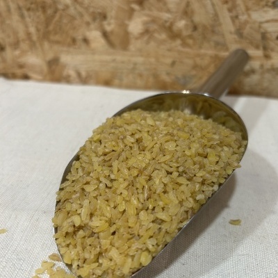 Colher metálica com bulgur amarelo claro em superfície branca