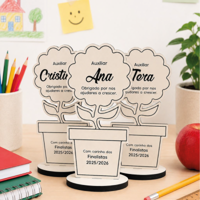 Três prémios em madeira em forma de flor com nomes, numa mesa com material escolar e desenhos ao fundo