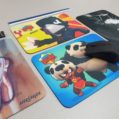 Quatro tapetes para rato com designs variados e um rato preto em cima de um deles