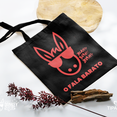 Saco de tecido preto com estampa vermelha de um burro e texto, em fundo branco com madeira e folha