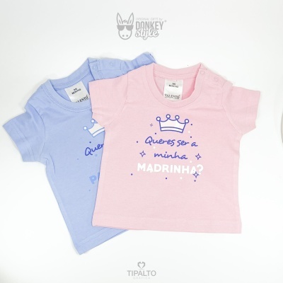 Duas t-shirts infantis azul e rosa com texto em português e uma coroa estampada