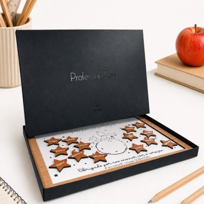 Caixa preta com placa decorativa personalizada para professor com nomes em estrelas de madeira ao lado de lápis e caderno