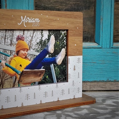 Moldura de fotografia em madeira com texto 'Miriam 2020' e padrão de árvores, com imagem de criança num baloiço