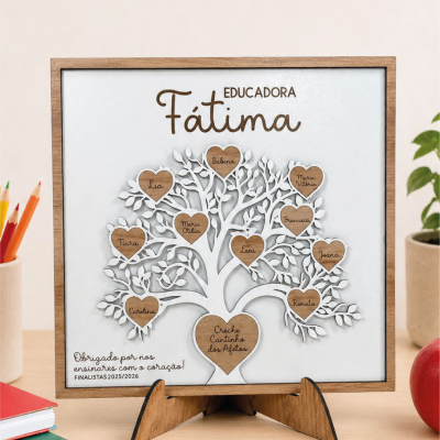Placa decorativa em madeira com árvore branca e corações castanhos com nomes e texto EDUCADORA Fátima e mensagem de agradecimento, sobre mesa com objetos escolares.