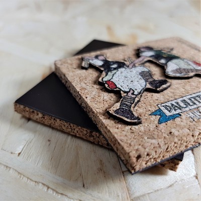 Suportes quadrados para copos em cortiça com figura decorativa e texto parcial sobre mesa de madeira clara