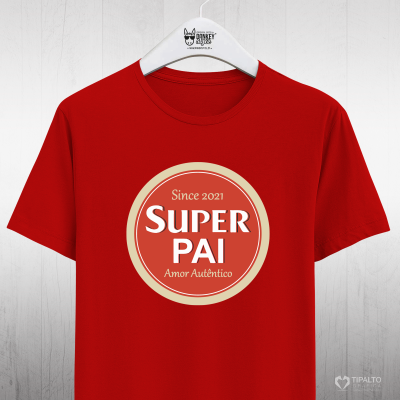 T-shirt vermelha com estampa redonda e texto 'Since 2021 SUPER PAI Amor Autêntico', pendurada num cabide branco.