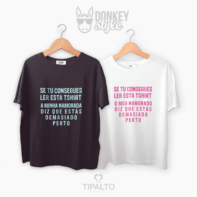 Duas t-shirts, preta e branca, com texto impresso em português sobre estar demasiado perto, penduradas em cabides.