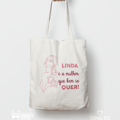 Saco de tecido branco com desenho e texto em vermelho, segurado por uma mão