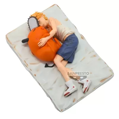 Figura de rapaz a dormir com um animal laranja com serrote na cabeça sobre colchão branco sujo