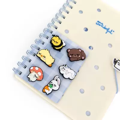 Pins de animais e cogumelo sobre cartão xadrez azul e caderno creme com furos