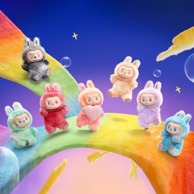 Conjunto de bonecos de pelúcia com orelhas de coelho em várias cores numa cena colorida com arco de pelúcia, estrelas e bolhas.