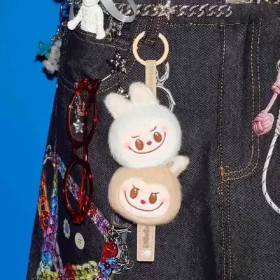 Chaveiro de peluche com duas caras sorridentes pendurado em calça de ganga preta
