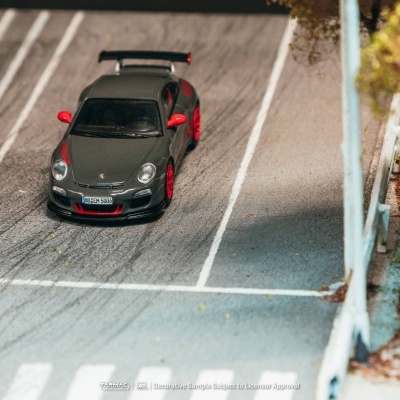 Miniatura de carro desportivo Porsche preto com detalhes vermelhos numa maqueta de estrada