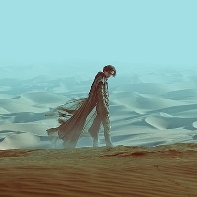 Pessoa com capa longa numa paisagem de dunas de areia