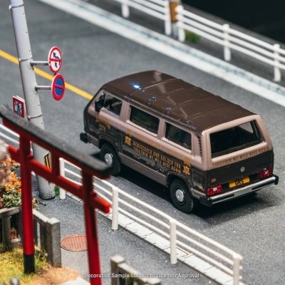 Miniatura de carrinha VW castanha e bege numa estrada com sinais de trânsito e decoração japonesa