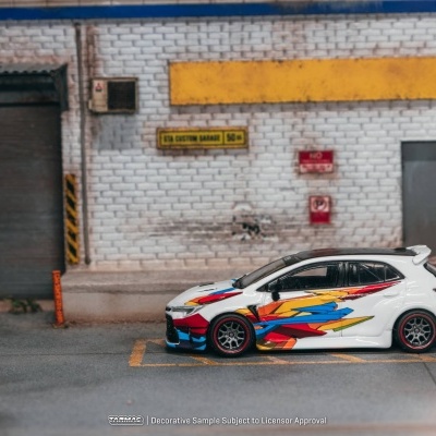 Miniatura de carro desportivo branco com padrões coloridos estacionado junto a parede de tijolos