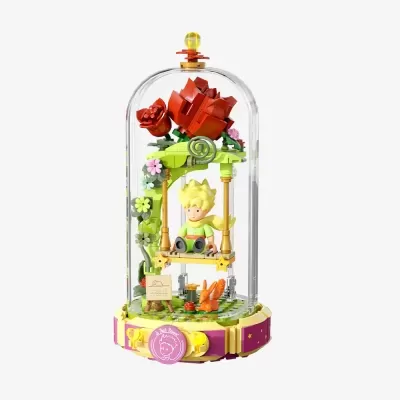 Figura do Pequeno Príncipe em baloiço sob cúpula com flores, base rosa e amarela com texto Le Petit Prince.