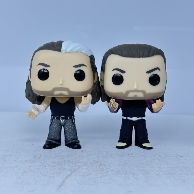 Duas figuras Funko Pop com cabelo e roupas diferentes, posando com gestos de mãos.