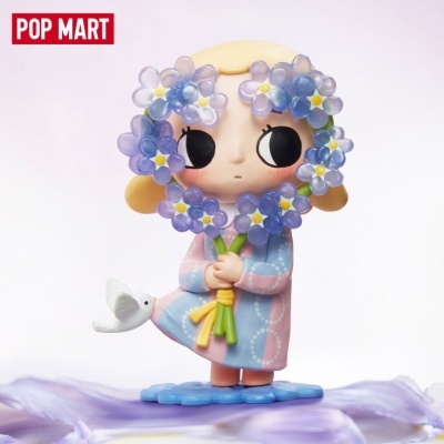 Figura de menina segurando flores lilases com pássaro branco, em vestido azul e rosa.