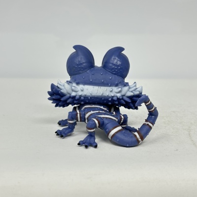 Figura colecionável azul de criatura com cauda e patas, vista de costas, fundo branco