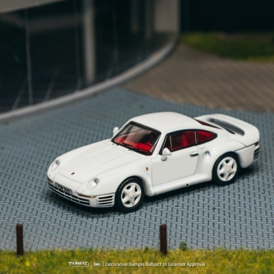 Miniatura de carro desportivo branco com interior vermelho numa superfície de calçada cinzenta.
