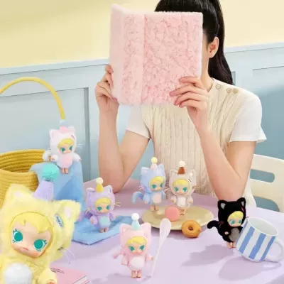 Bonecos de pelúcia de gatinhos coloridos com acessórios numa mesa lilás, com caneca e doces.