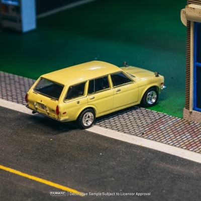 Miniatura de carrinha amarela clássica com jantes cromadas numa rua ao lado de edifício com janelas com publicidade