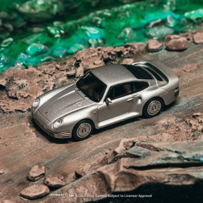 Modelo de carro desportivo prateado sobre superfície de terra e pedras junto a água verde