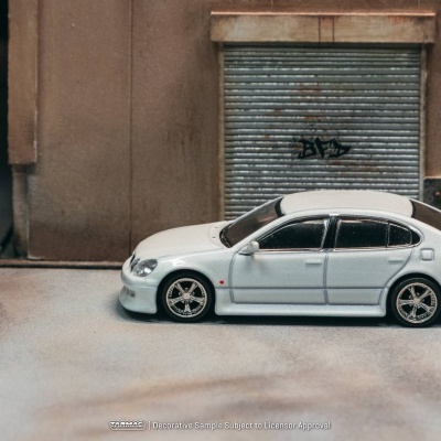 Miniatura de carro branco em frente a porta metálica com graffiti