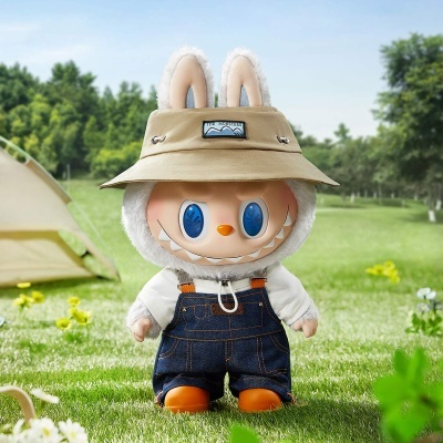 Boneco de peluche com jardineira, chapéu bege com o texto THE MONSTERS, em campo verde com tenda e árvores