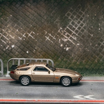 Miniatura de carro desportivo dourado em estrada com cerca metálica e parede em padrão losango