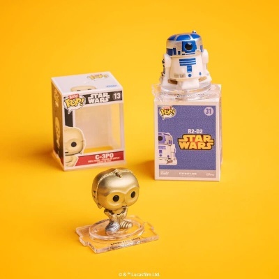 Duas figuras Pop! Star Wars, C-3PO dourado e R2-D2 azul e branco, com embalagem aberta em fundo amarelo.