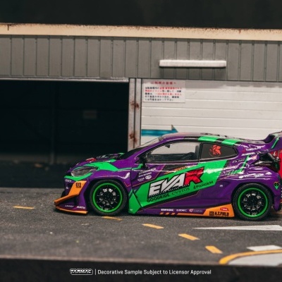 Carro de corrida em miniatura roxo e verde com decalques e pneus verdes junto a parede branca com sinais japoneses